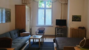 A furnished room with a sofa, a chair, a small table, a television, and a cabinet. - Apartment 'Am Park Sanssouci' (Potsdam)