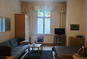A furnished room with a sofa, a chair, a small table, a television, and a cabinet. - Apartment 'Am Park Sanssouci' (Potsdam)