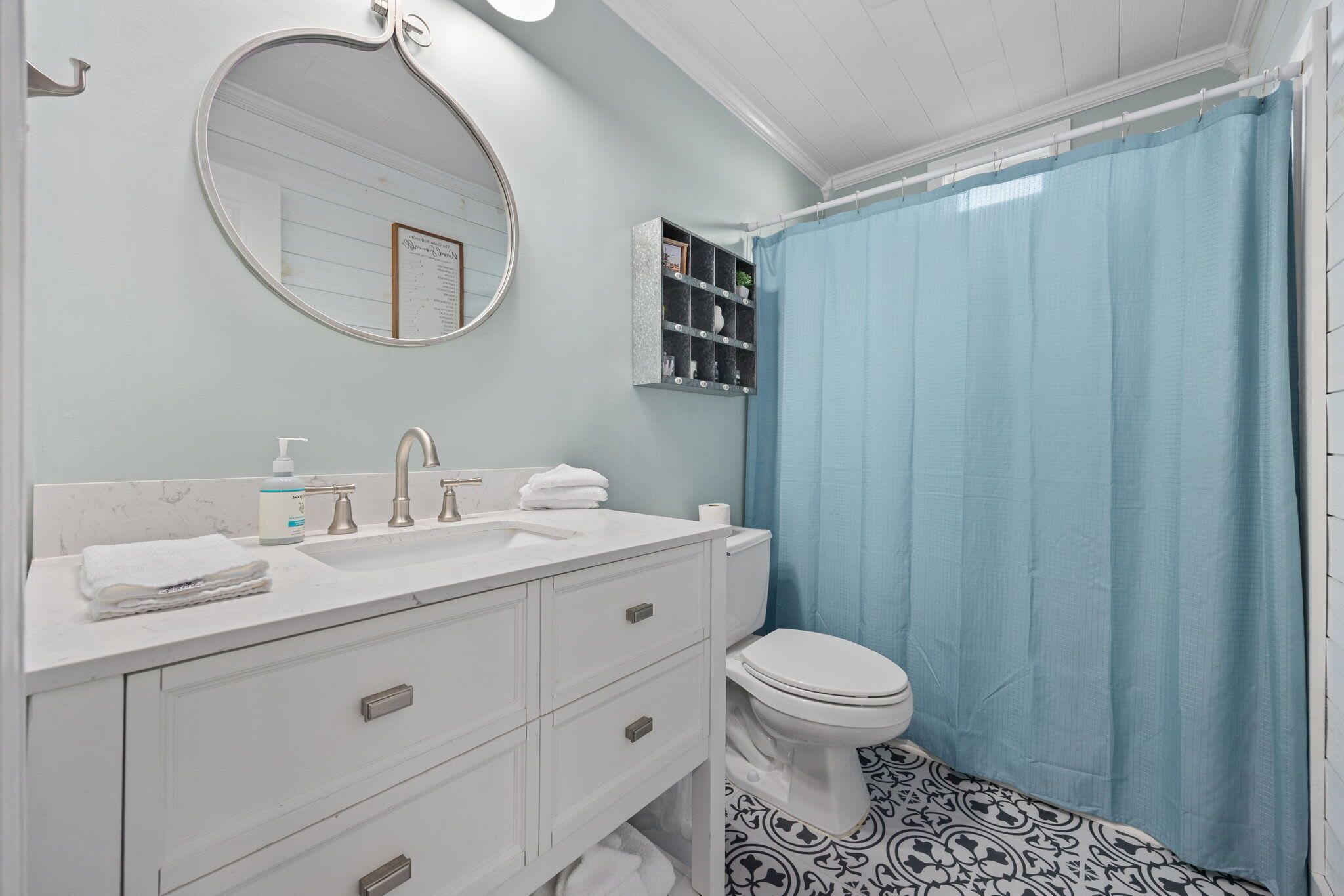 Une salle de bain avec un meuble-lavabo blanc, un miroir rond, des toilettes et un rideau de douche bleu.