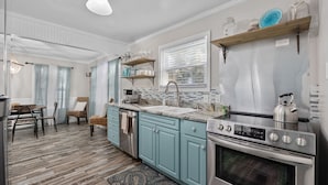 A kitchen with teal cabinets, a stainless steel oven, and a window with blinds.