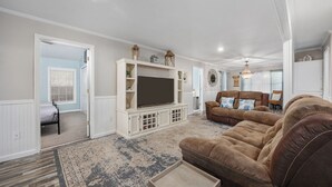 A spacious living room with a large flat-screen TV, a brown leather sofa, and a patterned rug.