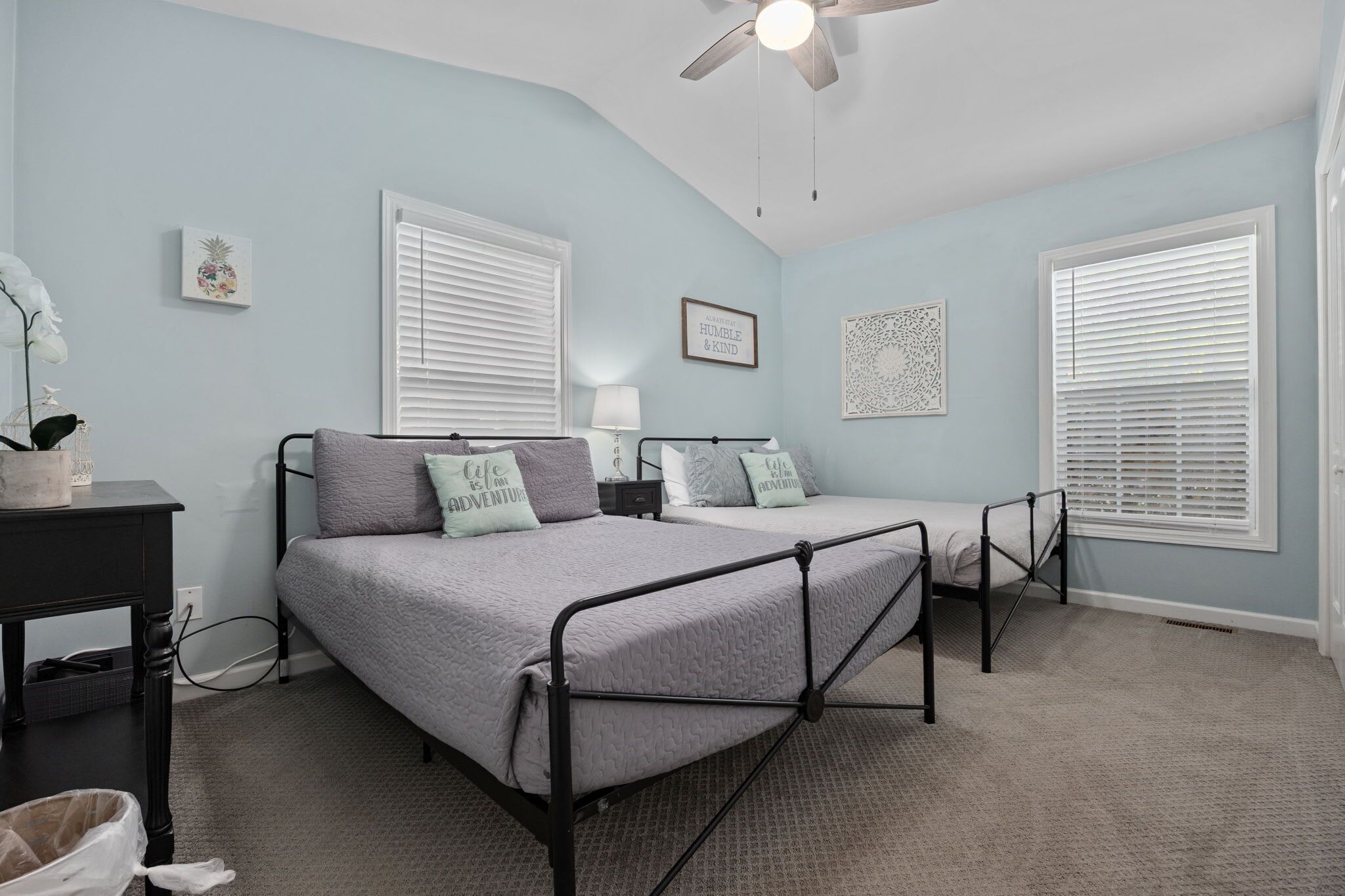A bedroom with two beds, a ceiling fan, and a window with blinds.