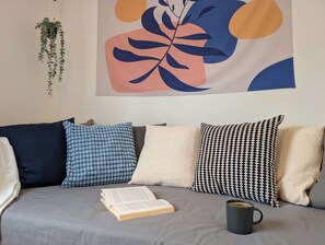 A sofa with patterned cushions, a hanging plant, a book, and a mug.