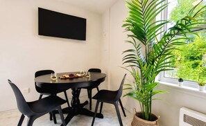 A dining area with a round table, black chairs, a potted plant, and a window with a view of greenery.