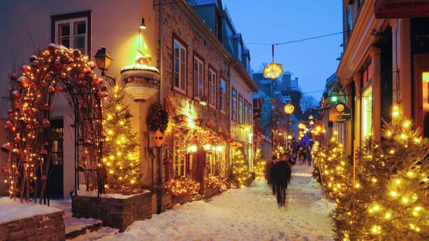 Una strada innevata fiancheggiata da edifici decorati con luci e addobbi natalizi.