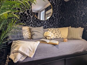 A bed with a grey bedspread, multiple pillows, a book, and a mug.