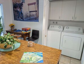 Un lavadero con lavadora y secadora, una mesa de comedor con un mapa, una silla y una planta en maceta.