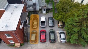 Un estacionamiento con varios coches aparcados en fila, al lado de un edificio con techo plano y un árbol a la derecha.