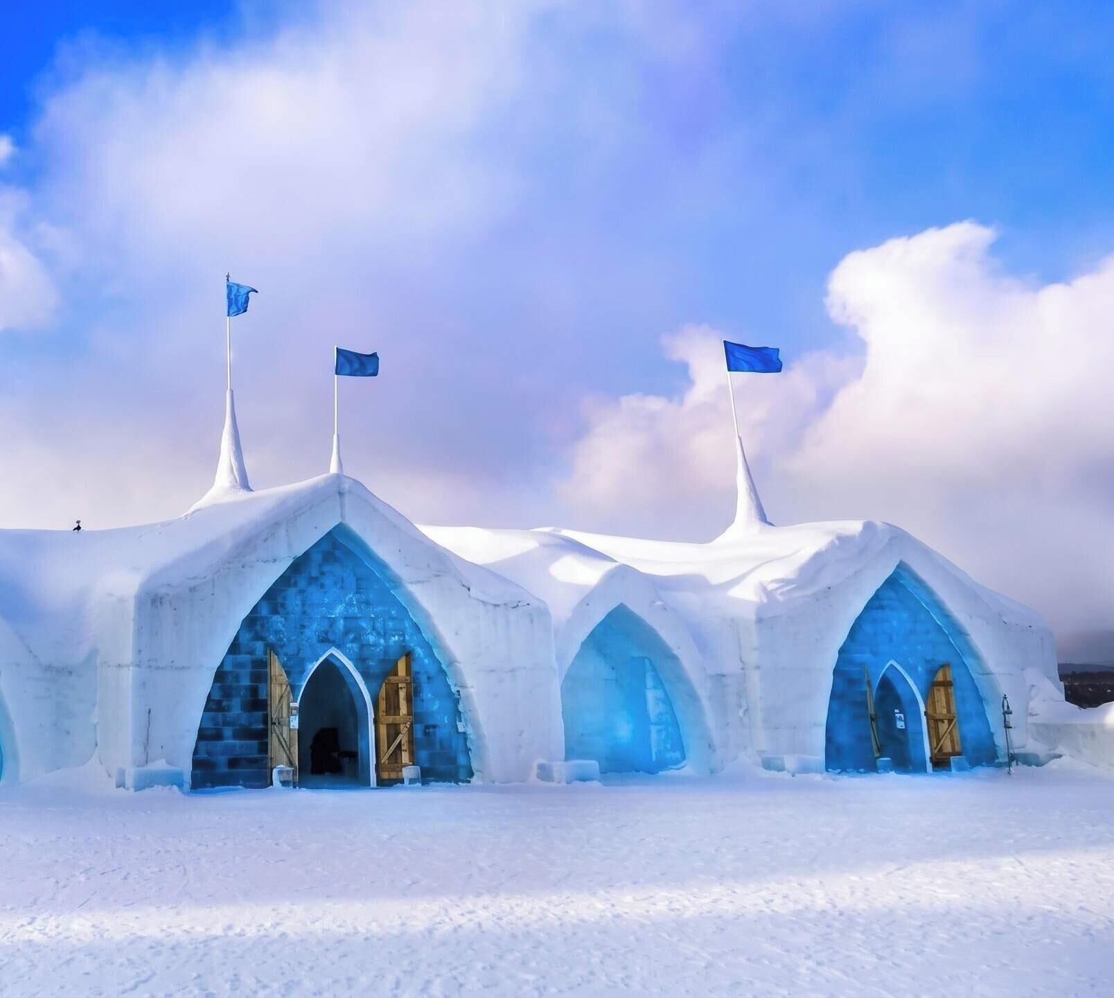 Tres estructuras tipo iglú con interiores azules y puertas de madera, situadas en un paisaje nevado.