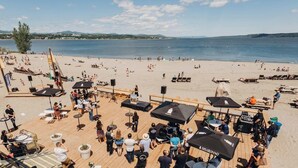 Un espacio junto a la playa con mesas al aire libre, sombrillas y un escenario para eventos.