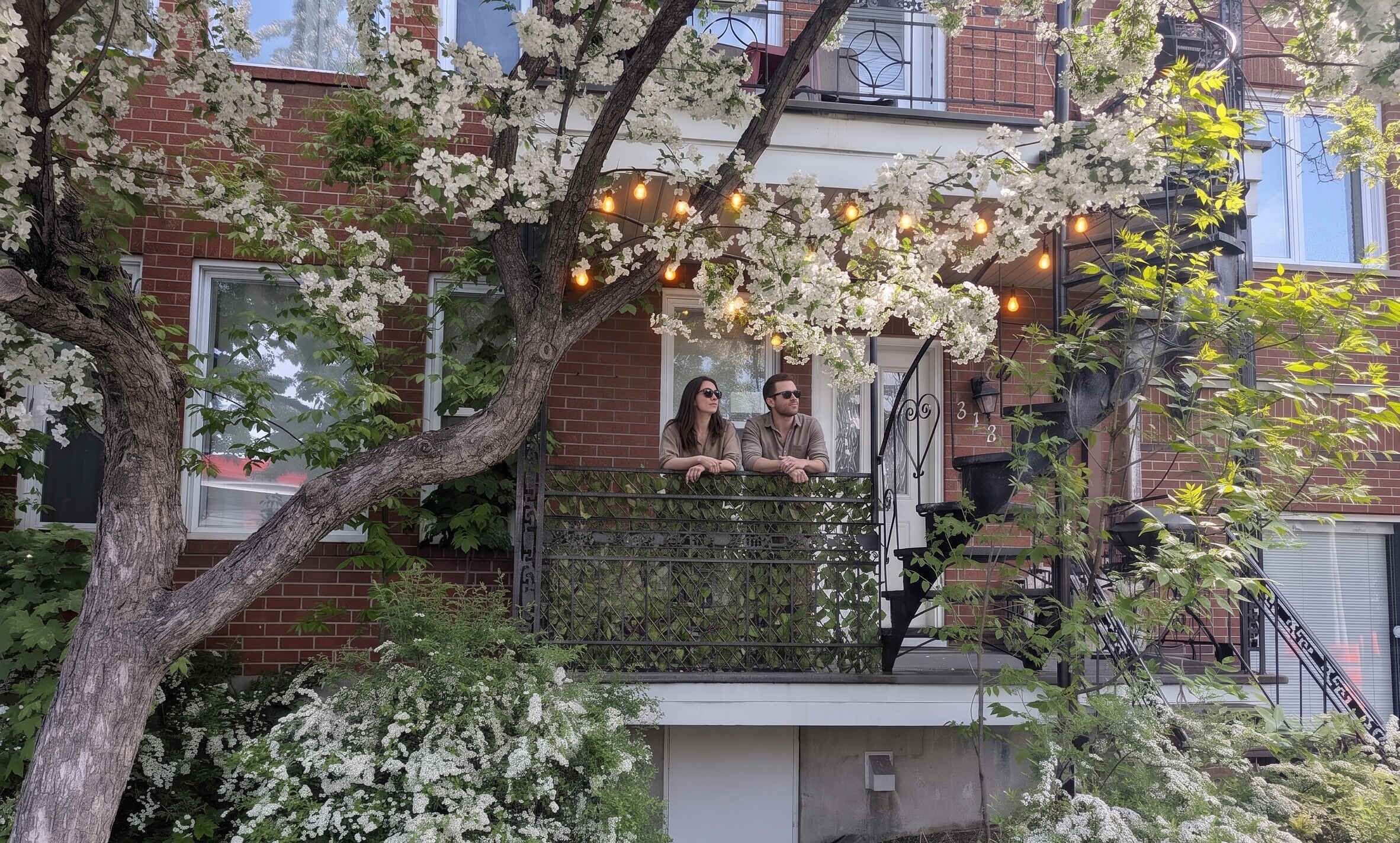 A residential building with a balcony, a tree with white flowers, and string lights.