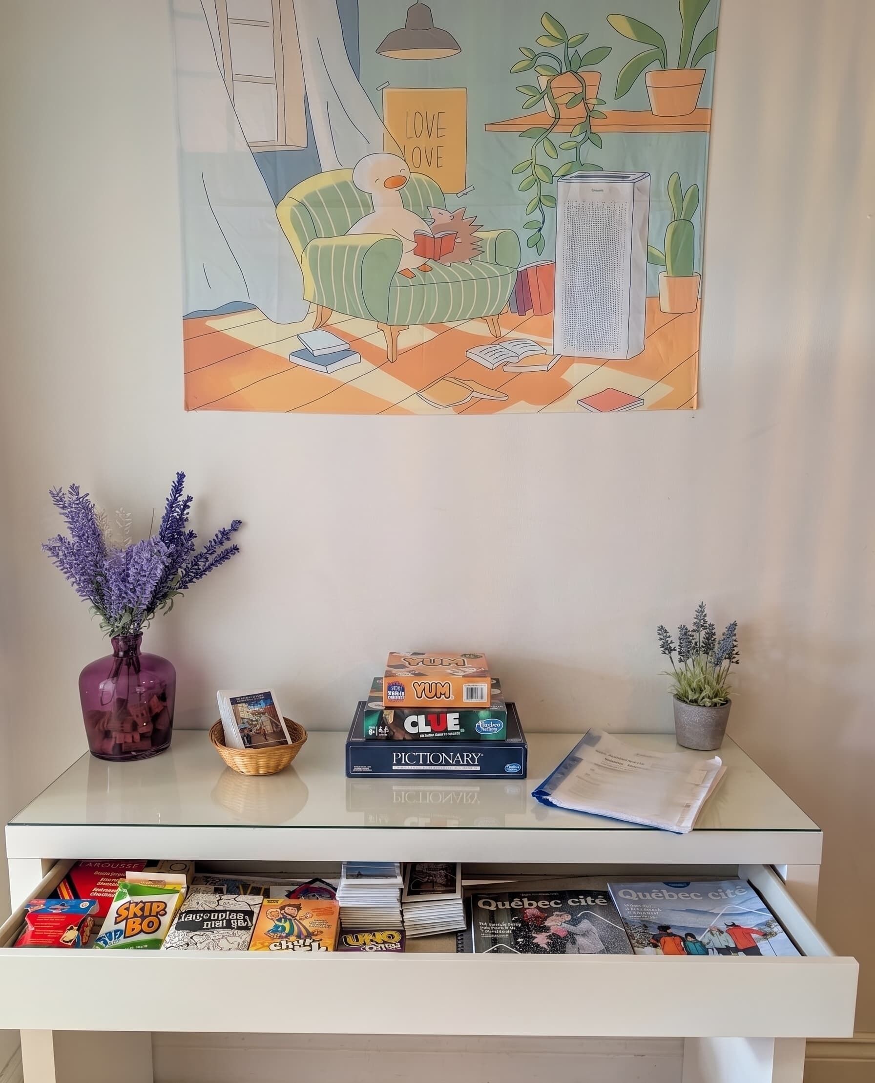 Una habitación con un escritorio de cristal, un cuadro, una planta en maceta y un libro titulado 'Clue'.