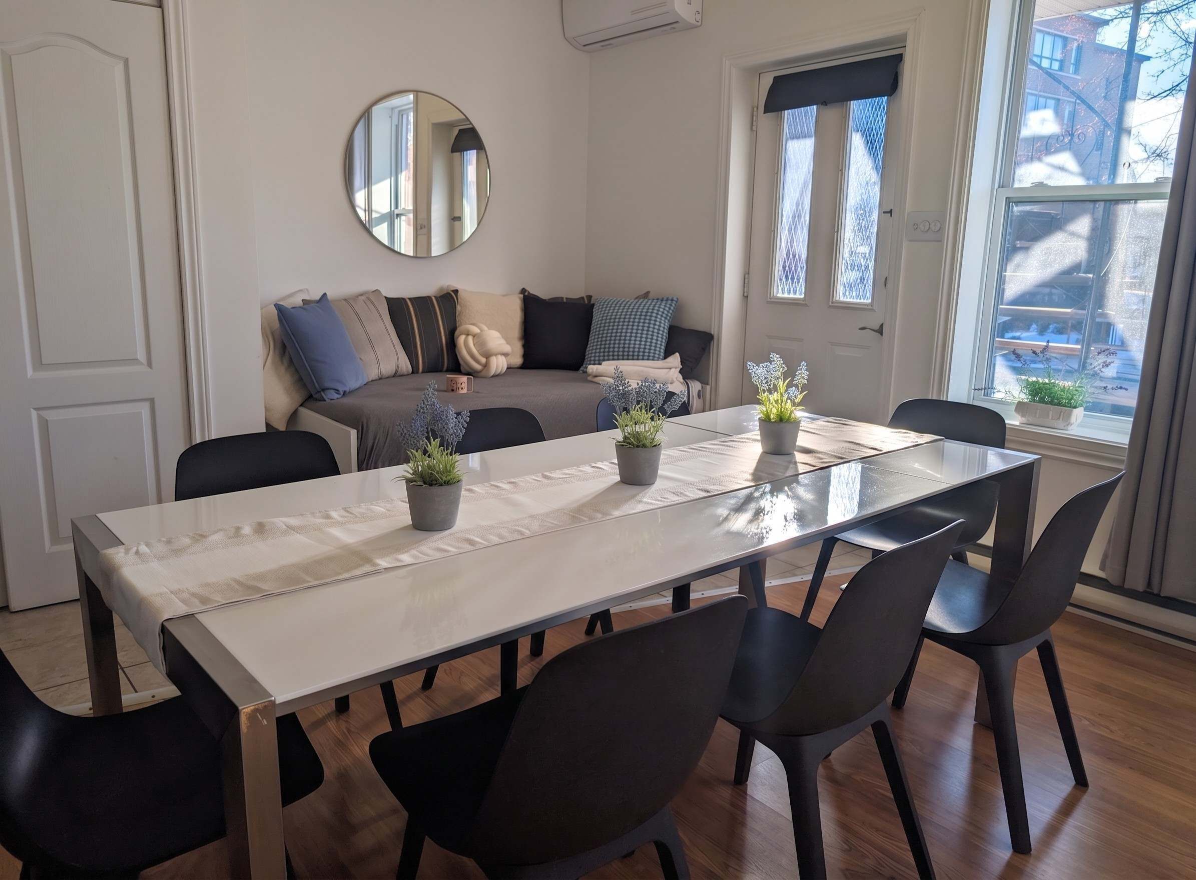 A dining area with a table, chairs, potted plants, a sofa, and a mirror.
