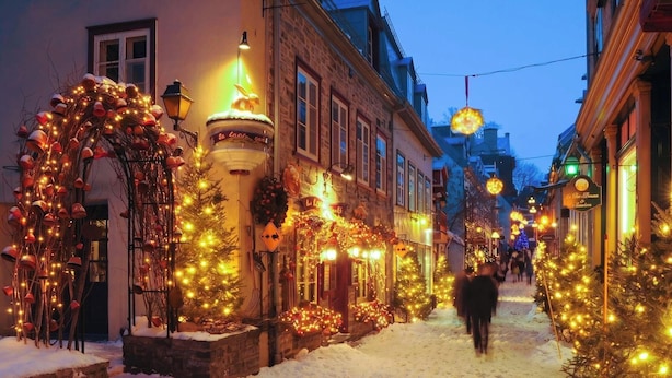 Una calle nevada flanqueada por edificios decorados con luces y adornos navideños.