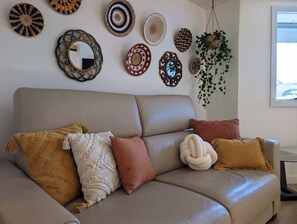 Un canapé beige agrémenté de coussins à motifs, un mur orné de tentures tissées et une plante suspendue.