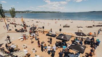 A beachside venue with outdoor seating, umbrellas, and a stage for events.