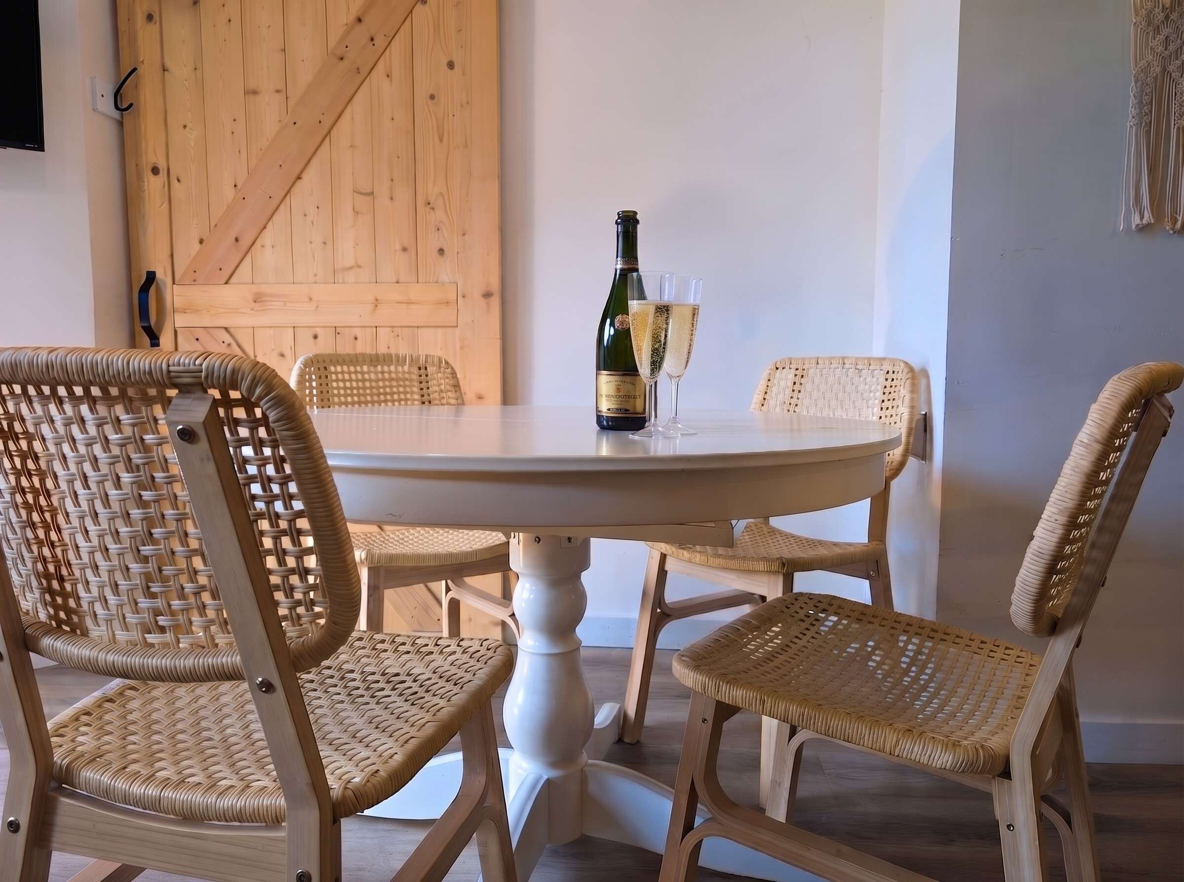 A round dining table with wicker chairs, a bottle of champagne, and two glasses on it.