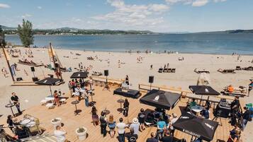 A beachside venue with outdoor seating, umbrellas, and a stage for events.