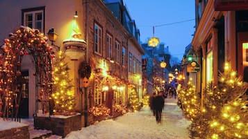 A snow-covered street lined with buildings adorned with Christmas lights and decorations.