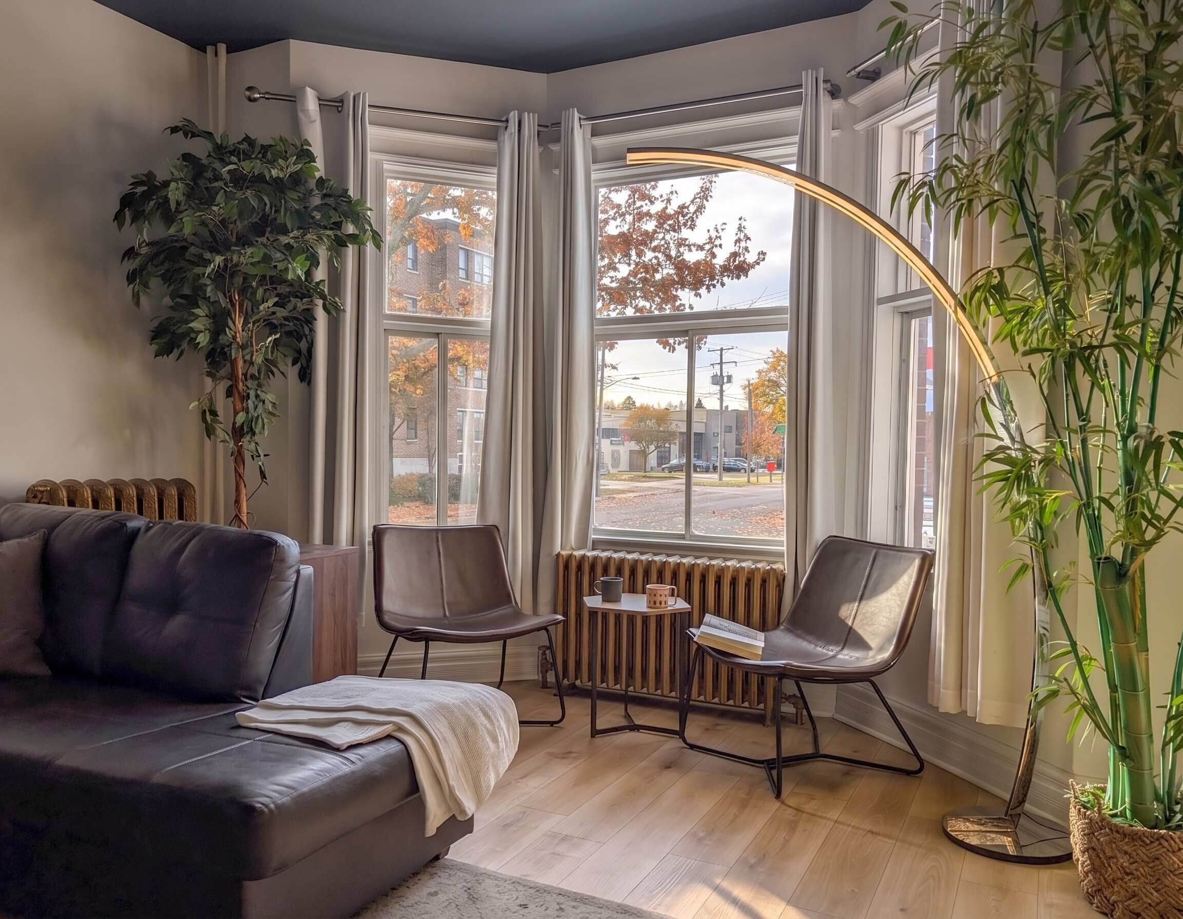 A modern living room with a leather sofa, two chairs, a small table, and a large window with curtains.