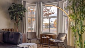 A modern living room with a leather sofa, two chairs, a small table, and a large window with curtains.