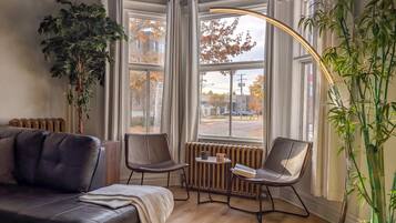 A modern living room with a leather sofa, two chairs, a small table, and a large window with curtains.