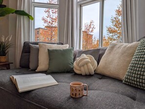 A cozy living room with a sofa, pillows, a book, and a mug.