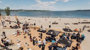 A beachside venue with outdoor seating, umbrellas, and a stage for events.