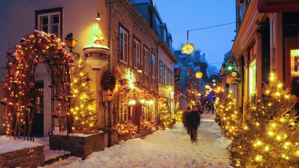 A snow-covered street lined with buildings adorned with Christmas lights and decorations.