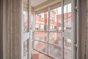A view through a window with a metal frame, a tiled floor, and a brick building in the background.
