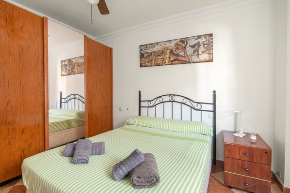 A bedroom with a bed, a wooden wardrobe, a nightstand, and a wall-mounted painting.