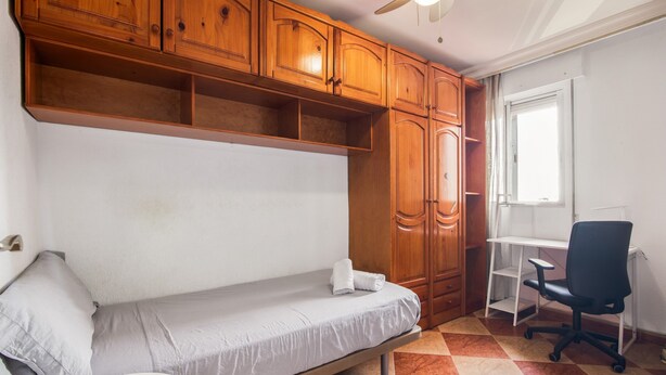 A single bed with a wooden headboard, a desk with a chair, and a window with curtains. - Apartment to Enjoy Huelva (Huelva)