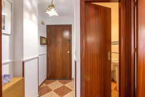 A hallway with a wooden door, a checkered floor, a light fixture, and a framed picture on the wall.
