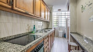 A kitchen with wooden cabinets, a granite countertop, a built-in stove, and a window providing natural light. - University Apartment (Huelva)