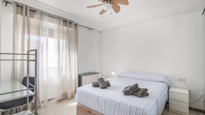 A hotel room with a bed, a desk, a chair, a nightstand, and a ceiling fan. - University Apartment (Huelva)