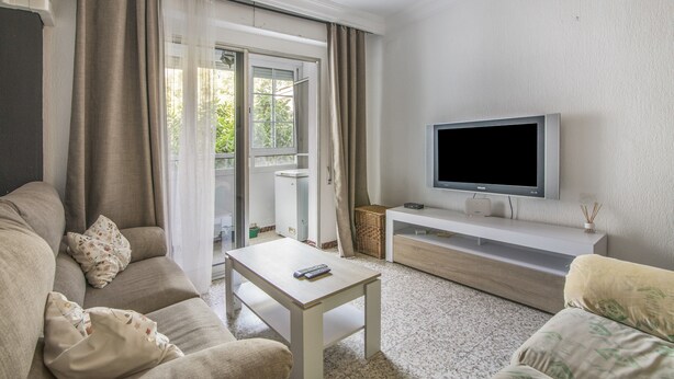 A living room with a sofa, a coffee table, a TV on a stand, and a sliding glass door. - University Apartment (Huelva)