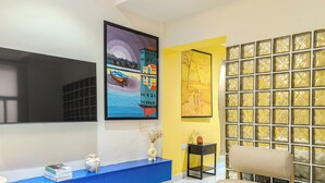 A room with a large flat-screen TV mounted on the wall, a blue console table with decorative items, and a yellow accent wall with a textured glass partition. - Glassvine (Lagos)