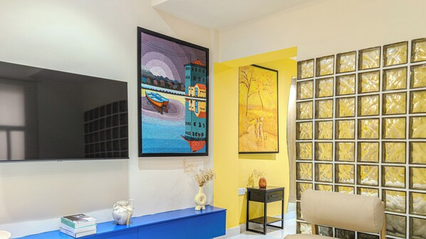 Une pièce dotée d’un grand téléviseur à écran plat fixé au mur, d’une console bleue agrémentée d’objets décoratifs et d’un mur d’accent jaune avec une cloison en verre texturé.