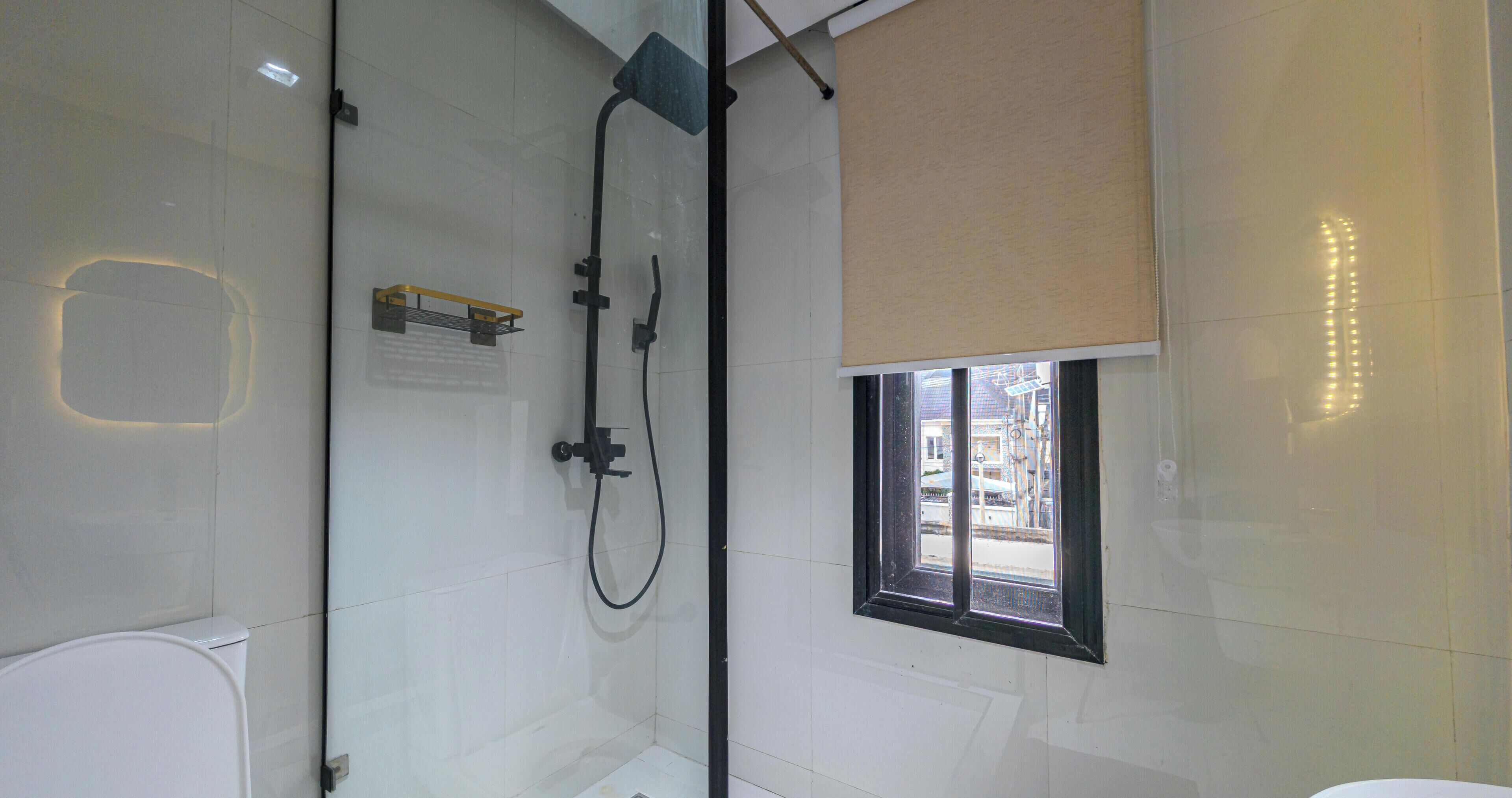 Ein modernes Badezimmer mit Duschkabine aus Glas, Toilette und Fenster mit Blick auf die Straße.
