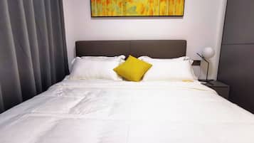 A neatly made bed with white linens and a single yellow pillow, a modern headboard, and a wall-mounted abstract painting.