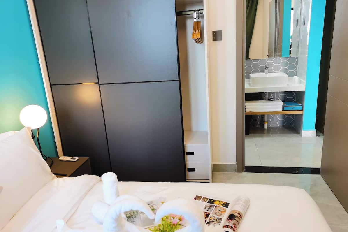 A hotel room with a bed, a nightstand with a lamp, a wardrobe, and a bathroom visible through an open door.
