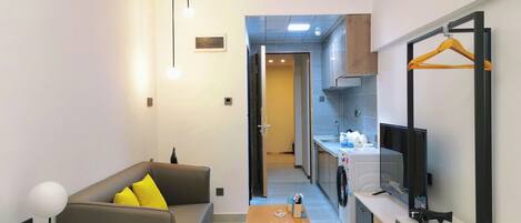 Una camera d'hotel moderna con divano, tavolo in legno, TV e angolo cottura completo di lavatrice.
