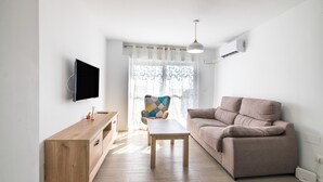 En moderne stue med en sofa, et træsofabord, et TV ophængt på væggen og et vindue med gardiner.