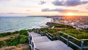 Eine Küstenstadt mit einer Treppe, die zu einem Aussichtspunkt mit Blick auf das Meer und einen Sonnenuntergang führt.