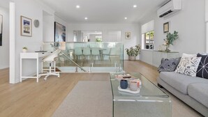 Ein modernes Wohnzimmer mit einem Glastisch, einem grauen Sofa und einer Treppe, die zu einer oberen Ebene führt.