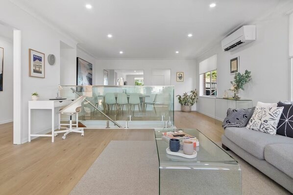 A modern living room with a glass coffee table, a grey sofa, and a staircase leading to an upper level.