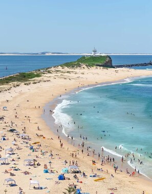 A beach with a lighthouse on a cliff, sandy shores, and clear blue waters.