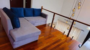 A grey sectional sofa with blue cushions in a room with wooden flooring and a glass railing overlooking a balcony.