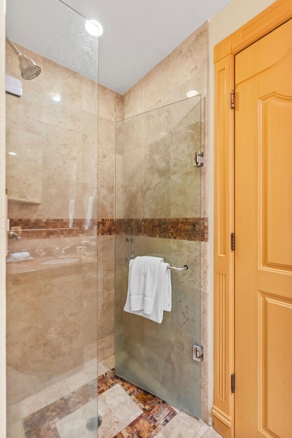 A glass-enclosed shower with a towel rack, a wooden door, and a tiled floor.