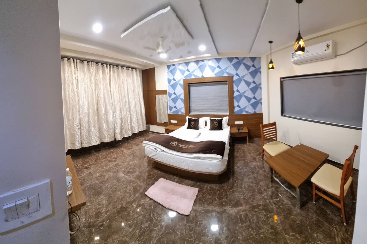 A hotel room with a bed, a desk, a chair, a large window, and a wall-mounted air conditioner.